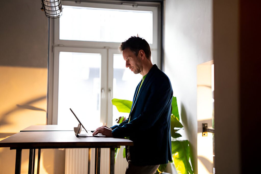 Home office desks for small spaces demonstrating a Businessman working on a tablet in a café with plants and natural light from his home office desk.